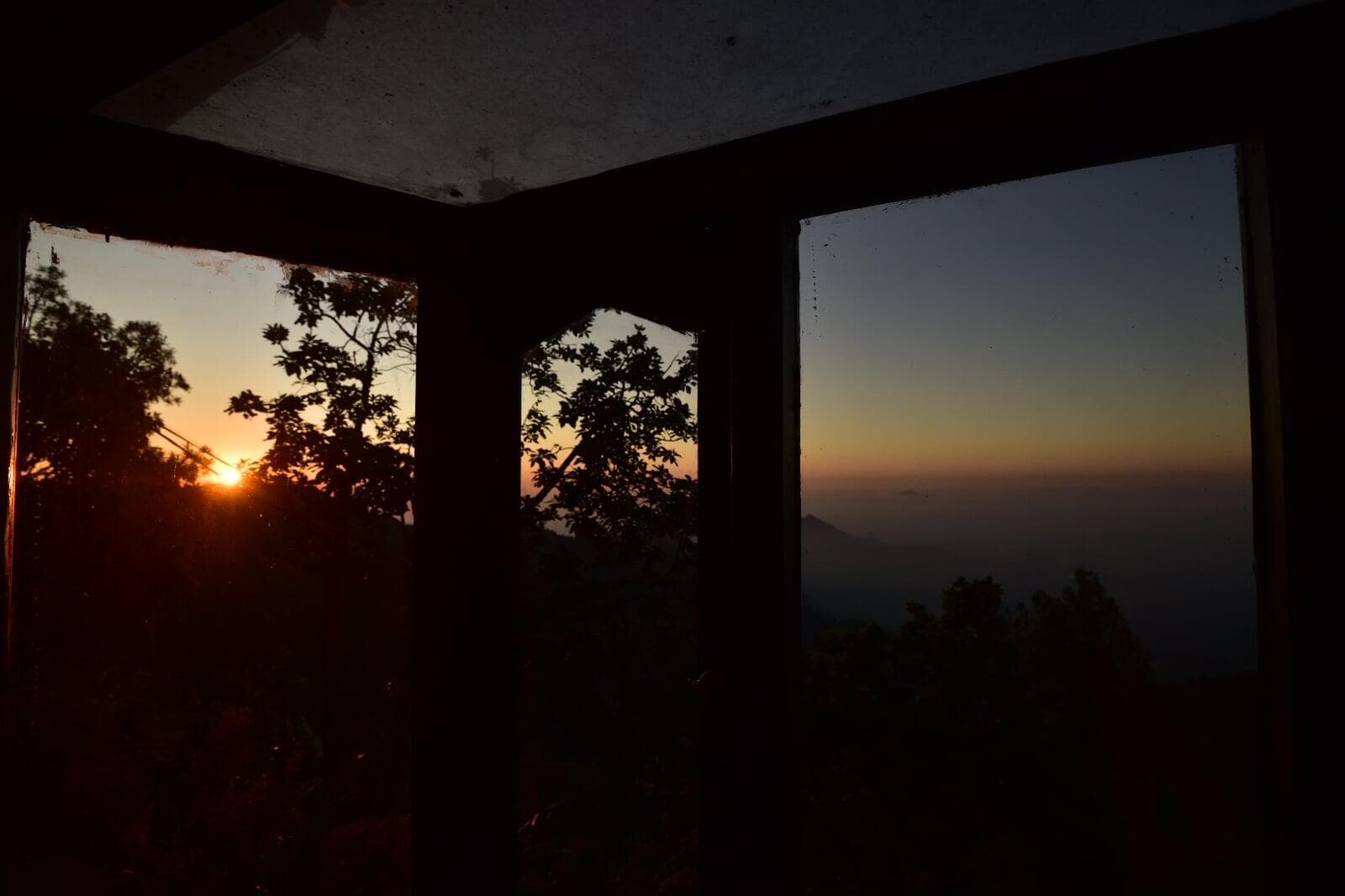 Sunrise seen through three wooden windows of a quiet farmhouse room, the Western Ghats beyond