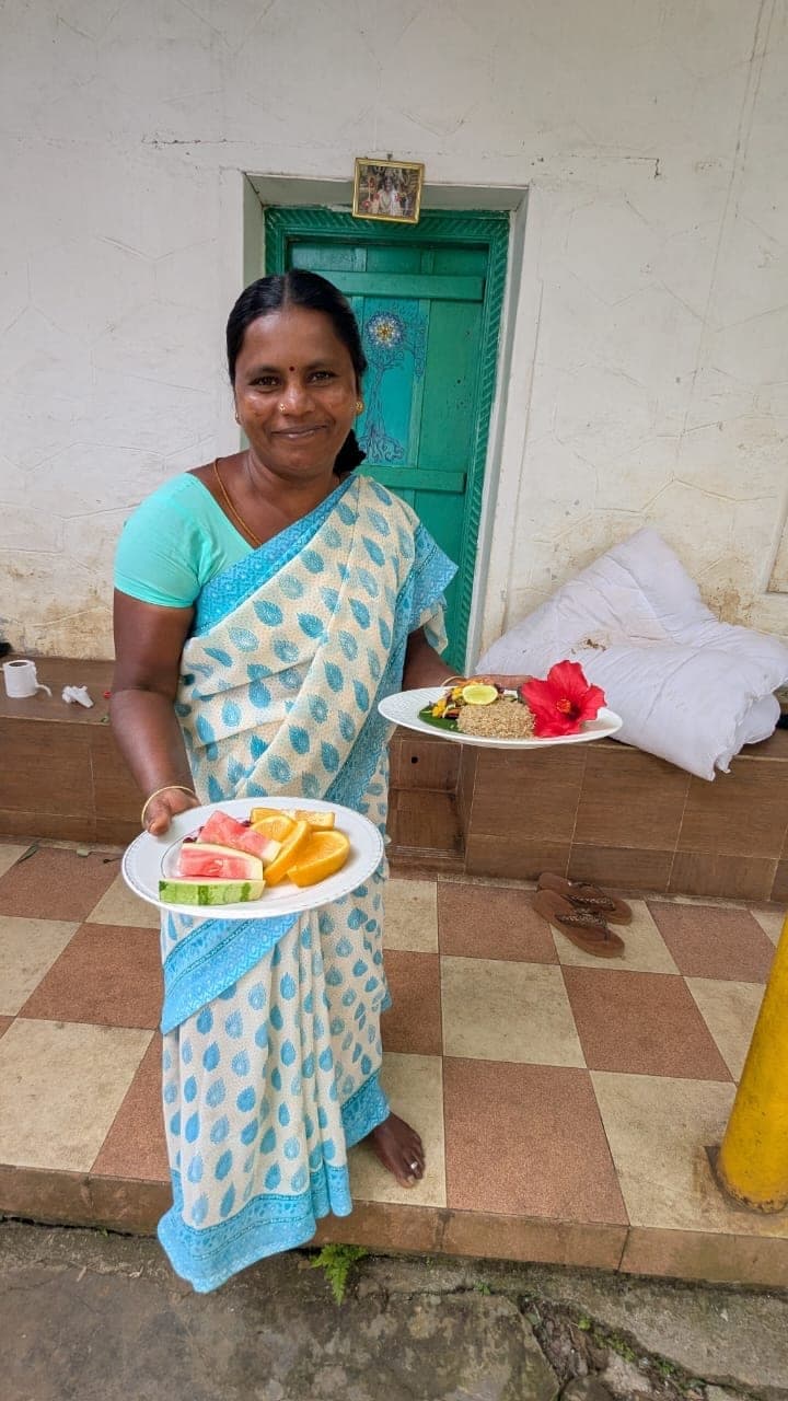 Rani Akka in a bright saree, carrying a plate of food by the kitchen door