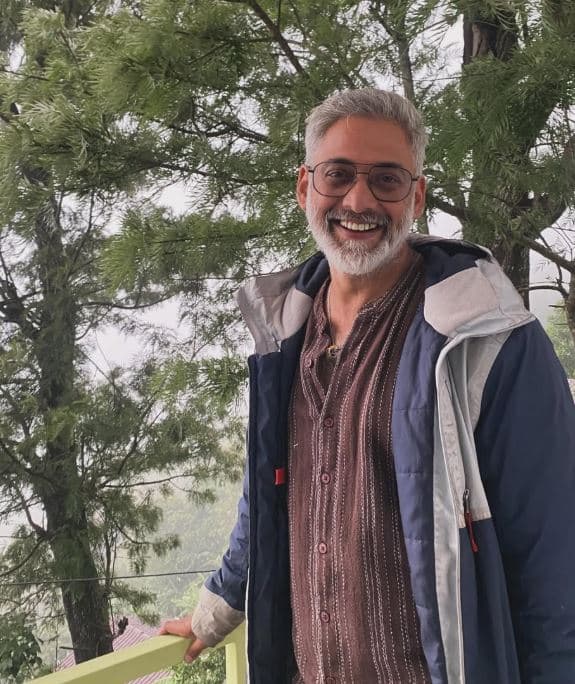 Vinay smiling on the terrace, the forest behind him