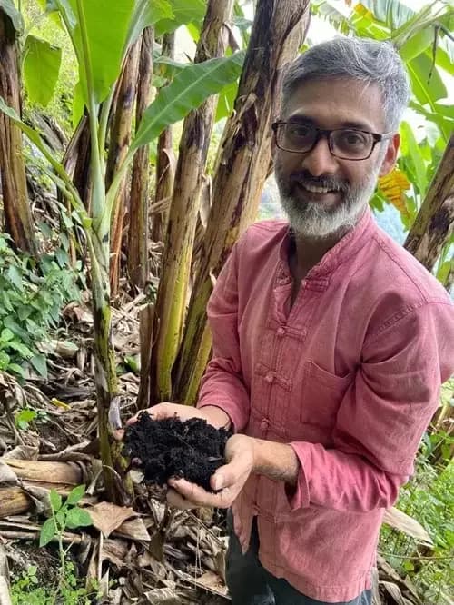 Vinay holding a handful of dark, living compost